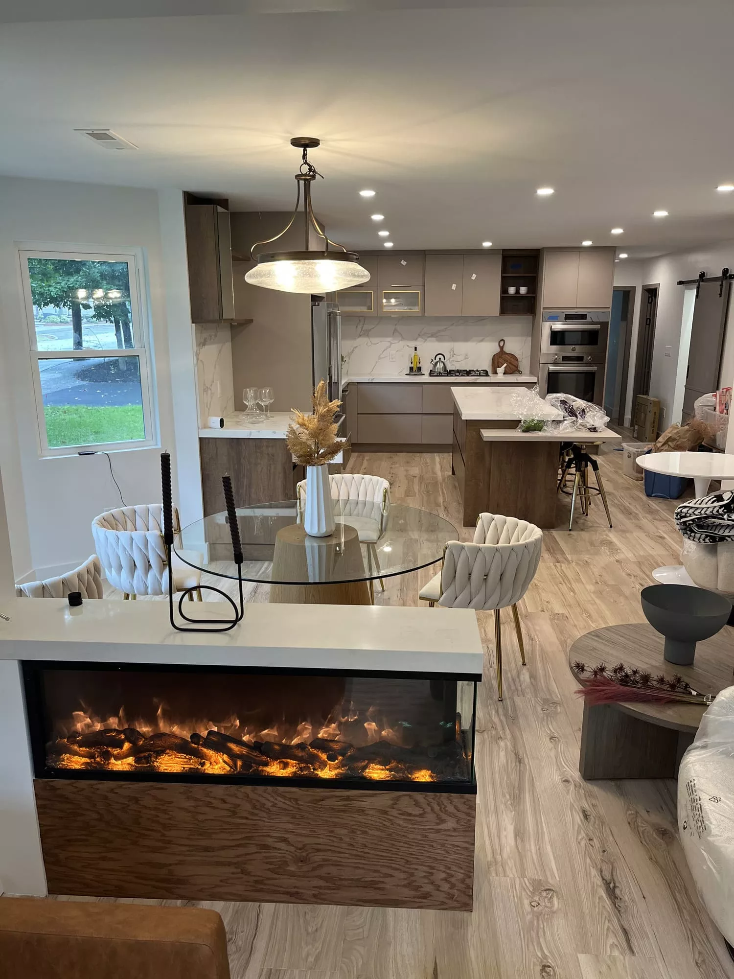 Fully remodeled open-concept kitchen and living room with modern cabinets, marble, electric fireplace, and light wood floors.