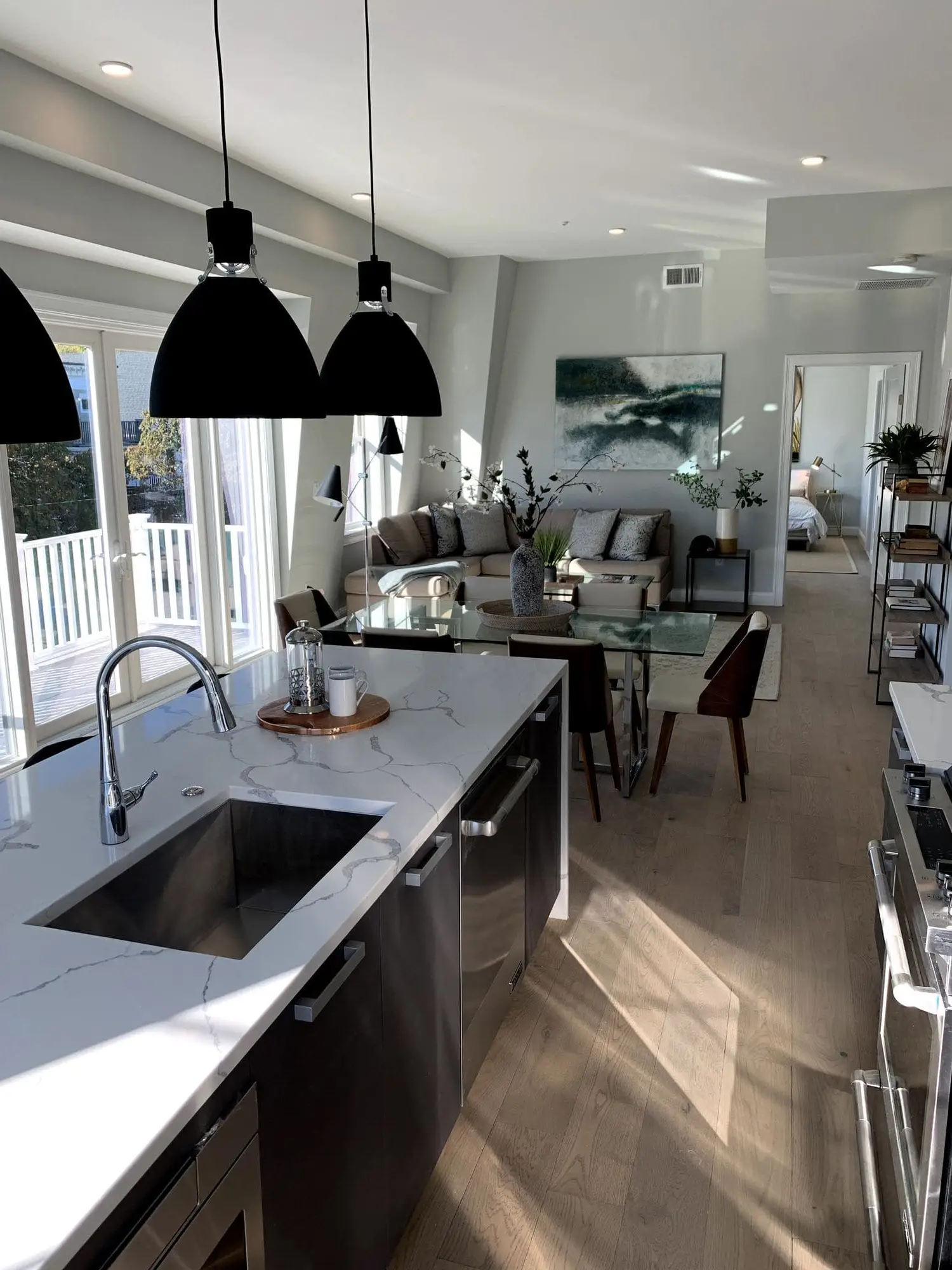 Modern kitchen with white marble-look island, dark cabinets, and stainless sink. Open concept living area with beige sofa,...
