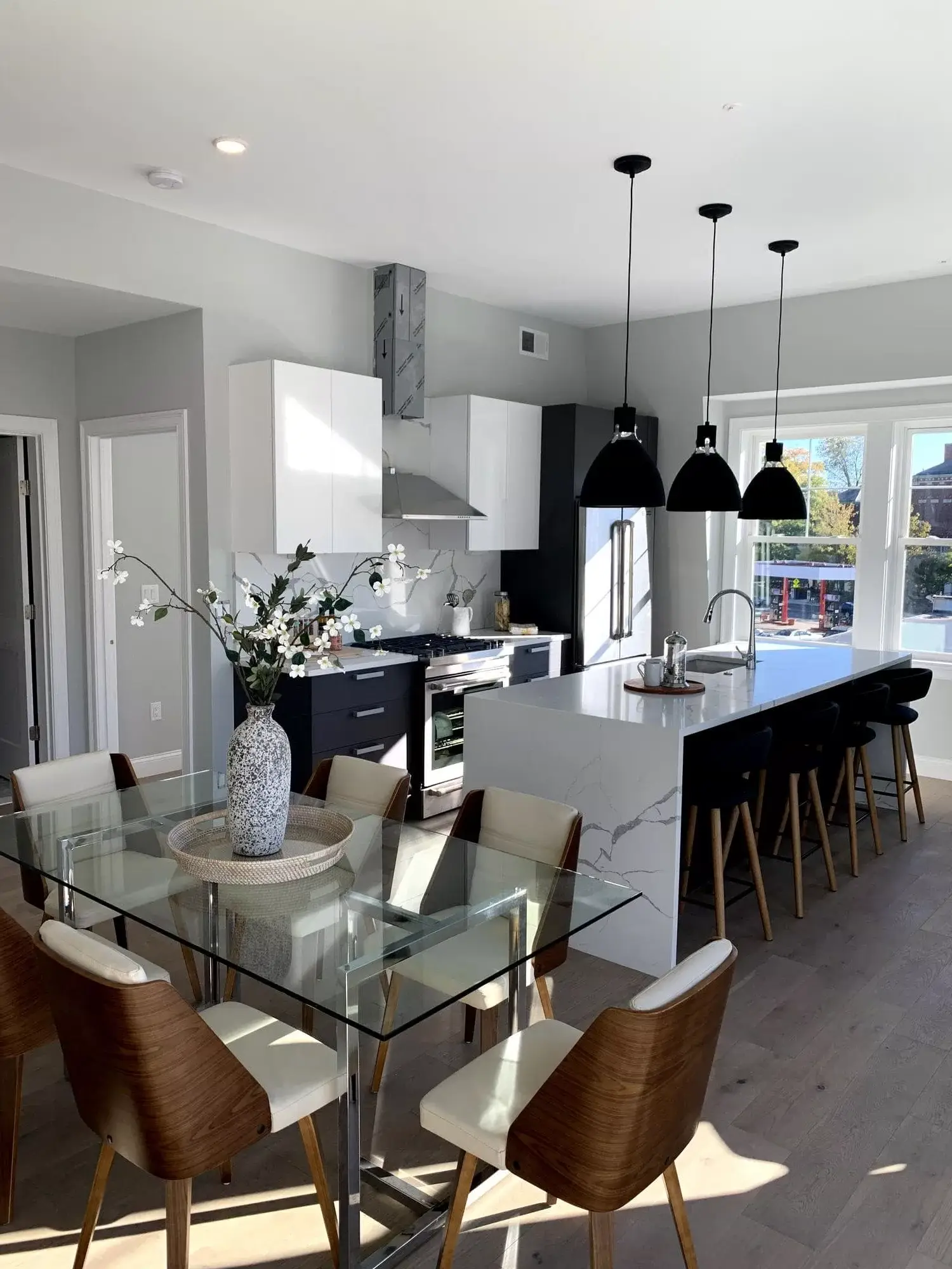 Stylish remodeled kitchen featuring white/black cabinets, large marble island, a glass dining table, and light hardwood fl...