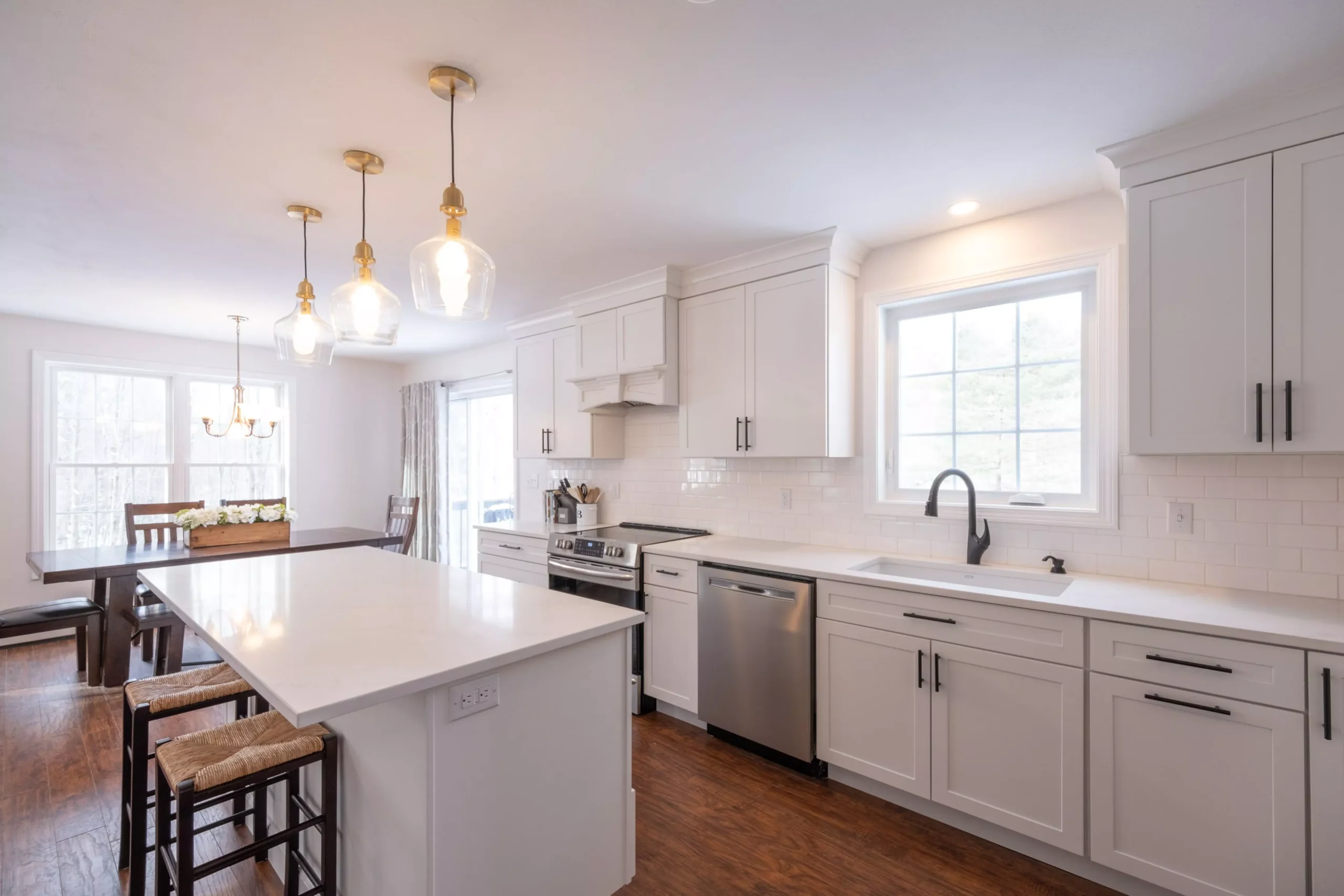 Bright, modern kitchen with white shaker cabinets, quartz countertops, stainless steel appliances, dark wood floor, and go...